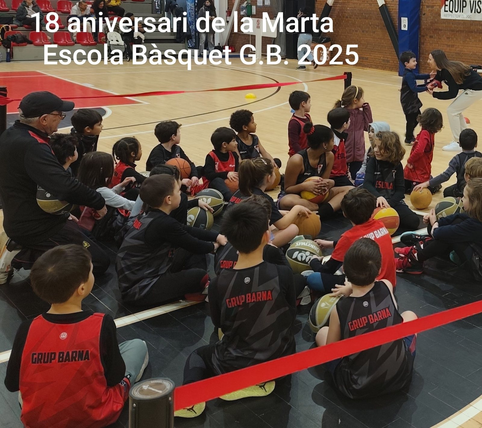 Els nens i nenes de l'Escoleta asseguts a la pista escoltant